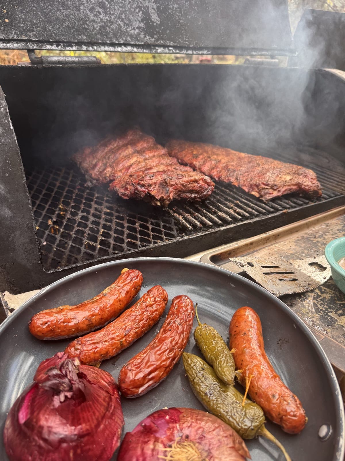 Ribs smoking on the grill with sausages and pickles